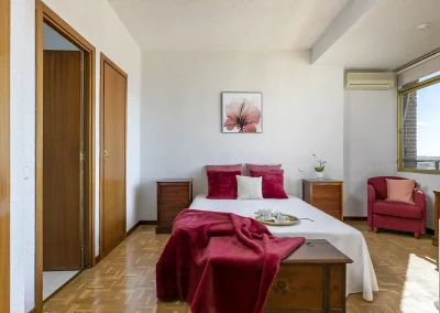 Imagen del dormitorio principal después del Home Staging, con textiles en color burdeos que combinan con las butacas ya existentes, creando un ambiente acogedor y armonioso.