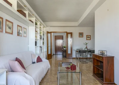 Imagen del salón después del Home Staging, destacando el vaciado y ordenación de estanterías y mobiliario, y el sofá renovado con una funda y textiles actuales.