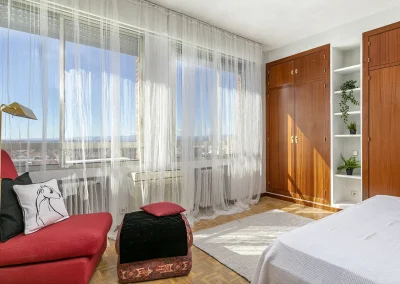Imagen del dormitorio individual después del Home Staging, con estores dañados retirados y sustituidos por cortinas que permiten ver la luz natural y las vistas de la vivienda.