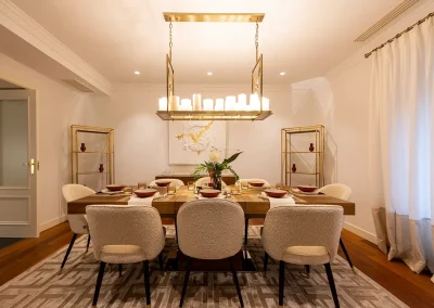 Detalle del comedor en vivienda de lujo en Madrid, mesa de nogal extensible para 10-12 personas, sillas tapizadas en bouclé y lámpara chandelier de lujo.
