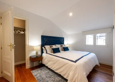 Dormitorio con cama king size, cabecero azul terciopelo y mesitas de noche de nogal en una vivienda premium de Madrid.